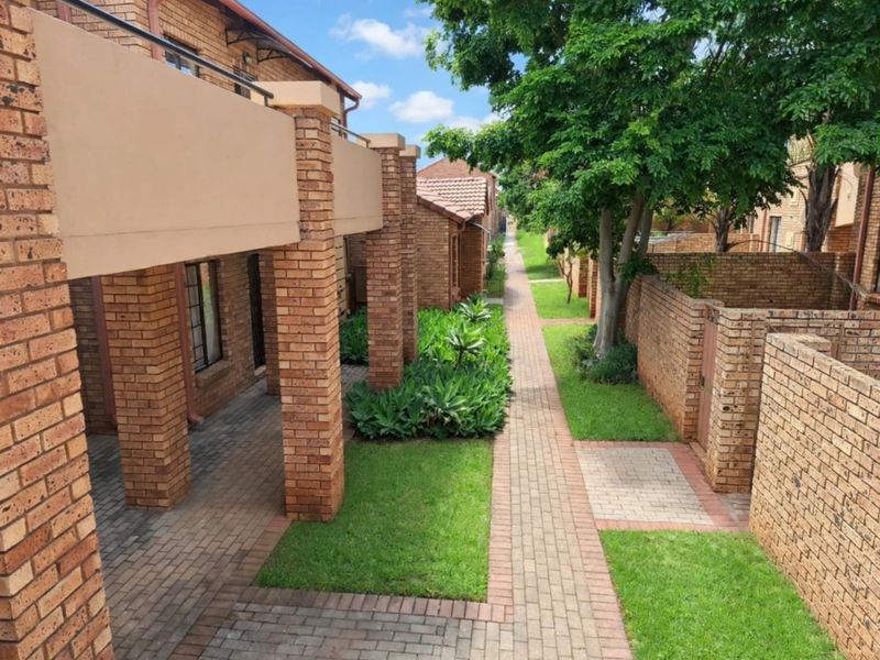 A well-maintained exterior view of the apartment complex featuring brick facades, covered patios, paved walkways, and established garden areas.