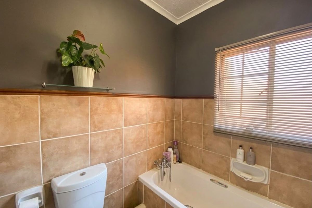 A functional bathroom featuring a bathtub, toilet, and neutral-toned wall tiling with a window providing natural light.