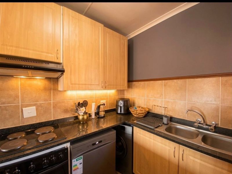 Compact kitchen featuring light wood cabinetry, granite countertops, a double stainless steel sink, and a built-in electric stove with an extractor fan.