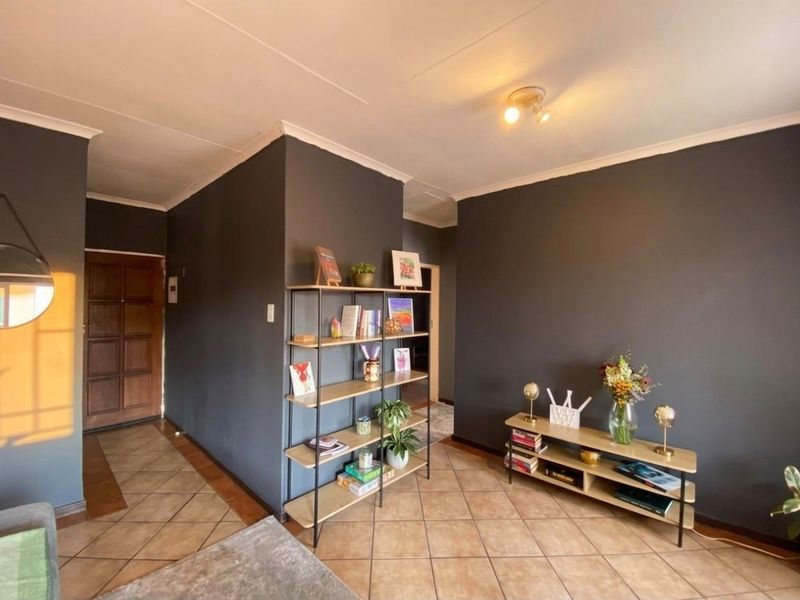 A living area featuring dark painted walls, tiled flooring, and a coved ceiling, providing a neutral base for interior design updates.