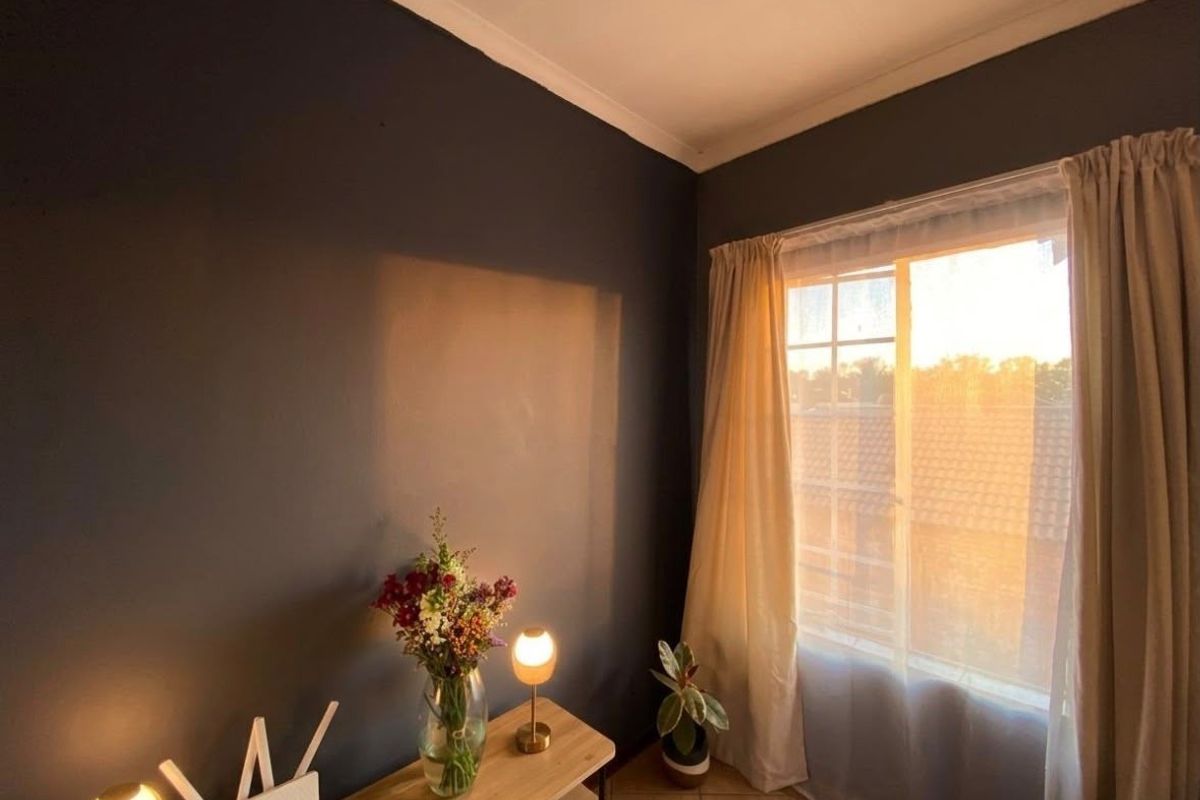 A cozy bedroom featuring dark painted walls, tiled flooring, and a window with natural light, creating a warm and inviting atmosphere.