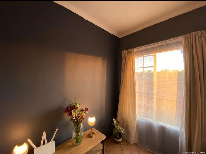 A cozy bedroom featuring dark painted walls, tiled flooring, and a window with natural light, creating a warm and inviting atmosphere.