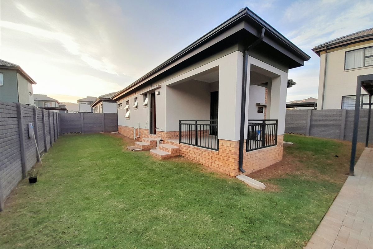 Rear view of the property featuring a covered patio, brick boundary walls, and a well-maintained lawn area.