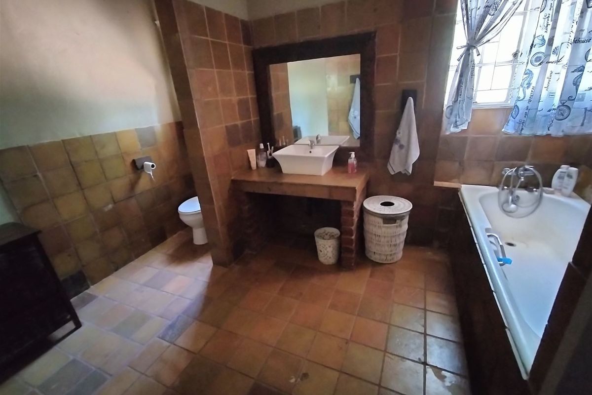 A rustic-style bathroom featuring terracotta-toned floor and wall tiles, a built-in vanity with a vessel sink, and a standard bathtub.