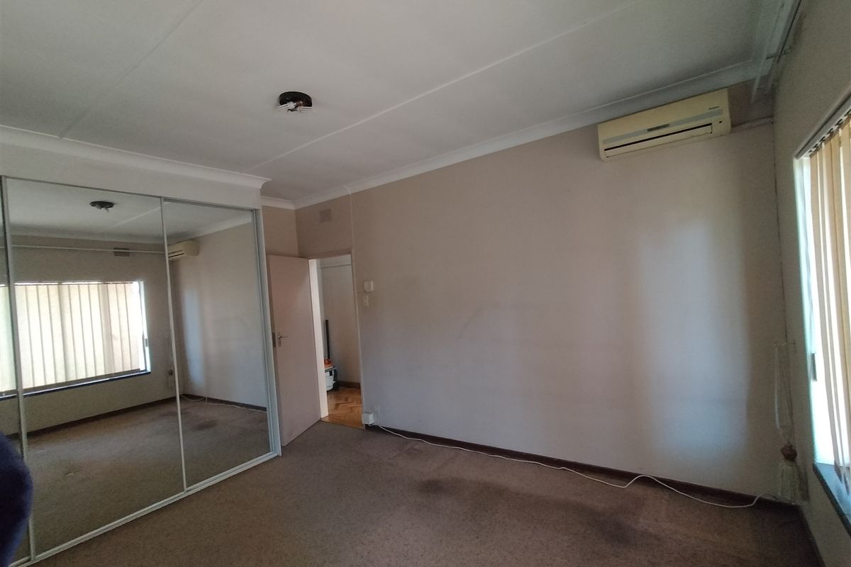 A spacious bedroom featuring a large mirrored sliding wardrobe, split-system air conditioning, and vertical blinds, offering a blank canvas for renovation.