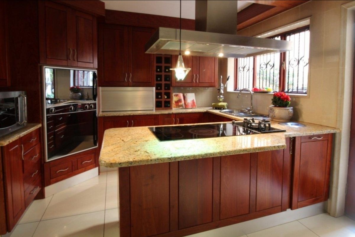 A well-appointed kitchen featuring rich wood cabinetry, granite countertops, a central island with dual hobs, and a stainless steel extractor fan.