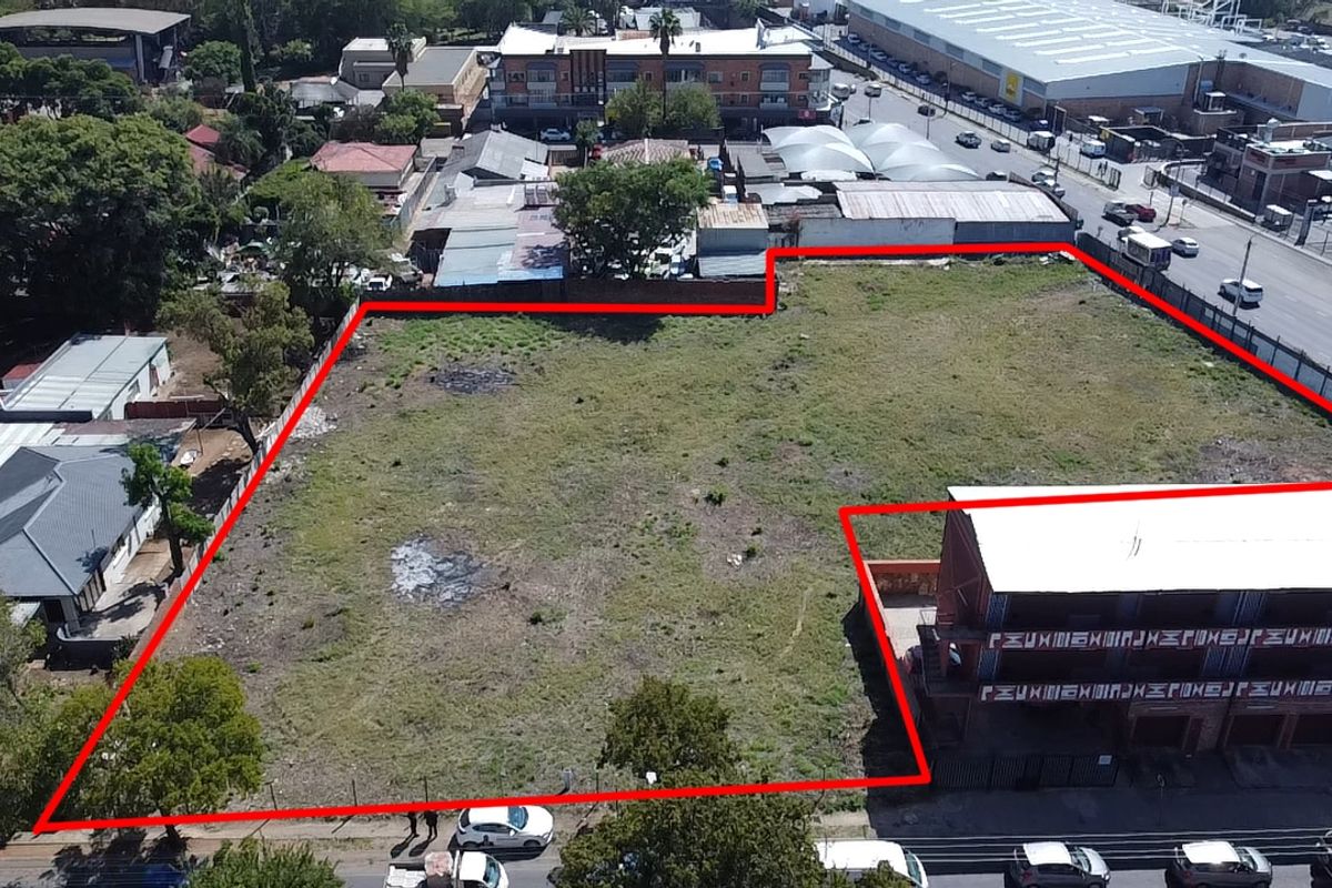 Aerial view of a vacant commercial land plot with perimeter fencing, situated in a developed urban area.