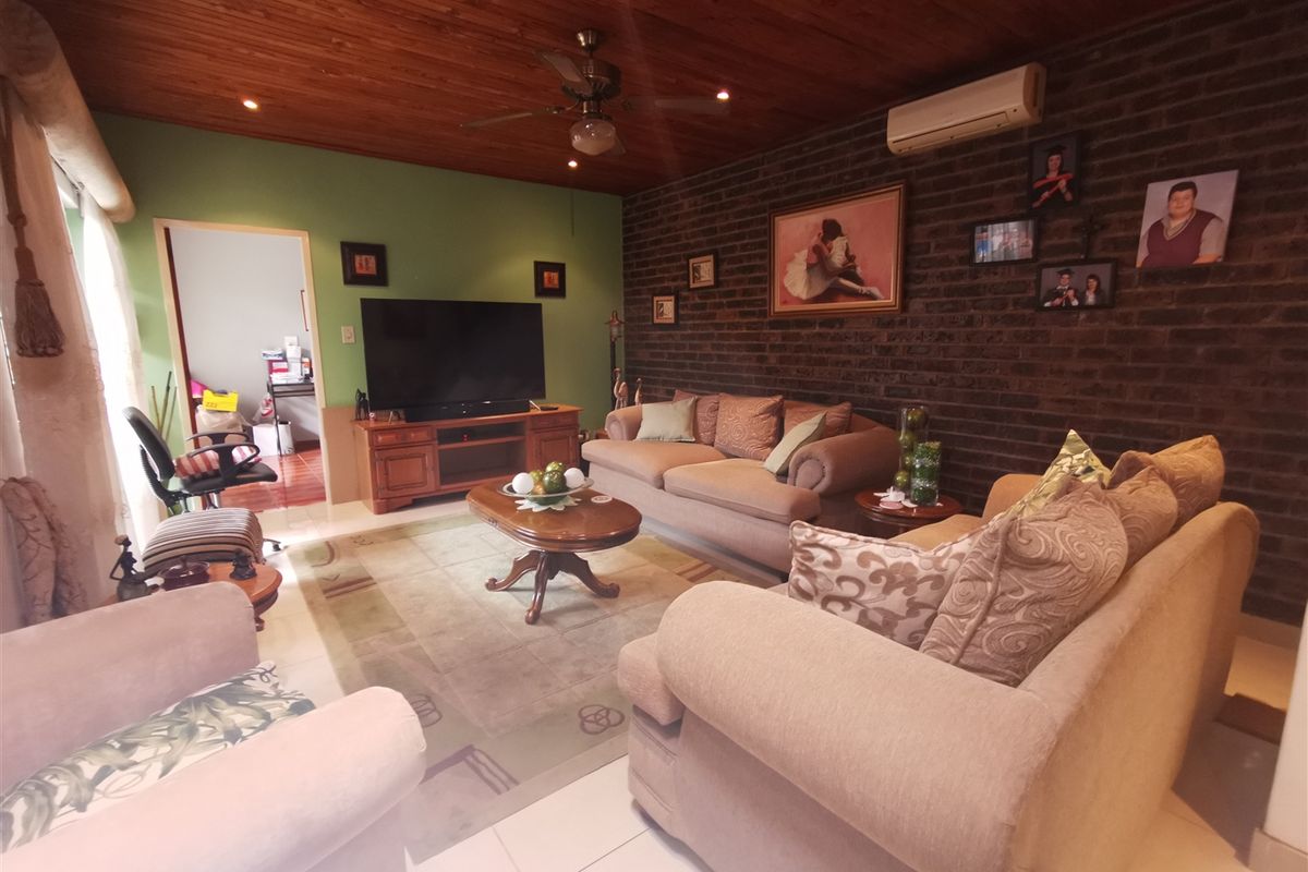 A living room featuring a timber ceiling, exposed brick feature wall, tiled flooring, and a split-system air conditioner.