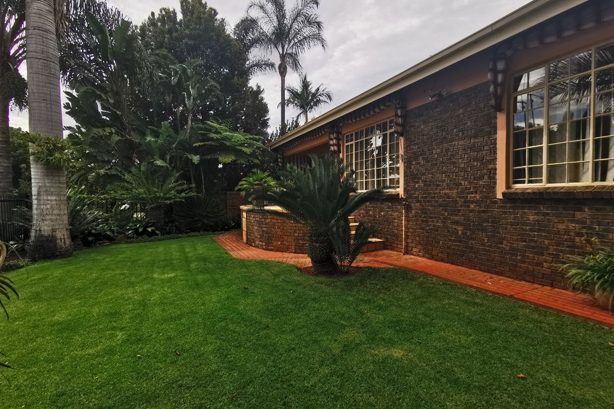 A well-maintained rear garden featuring a brick facade, paved walkway, and established landscaping with a lush green lawn.