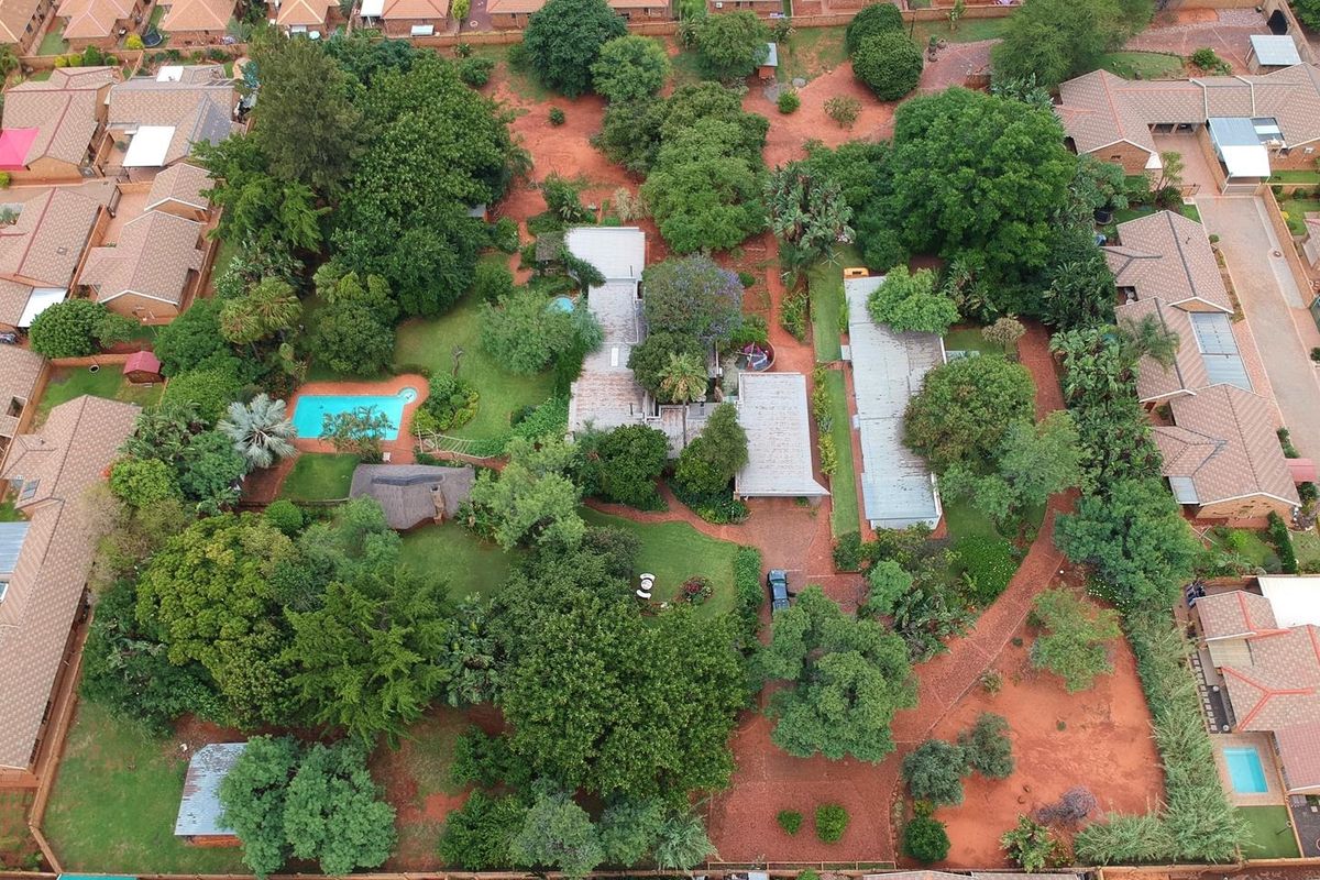 Aerial view of a spacious small holding property featuring a swimming pool, extensive mature gardens, and multiple residential structures within a residential estate.