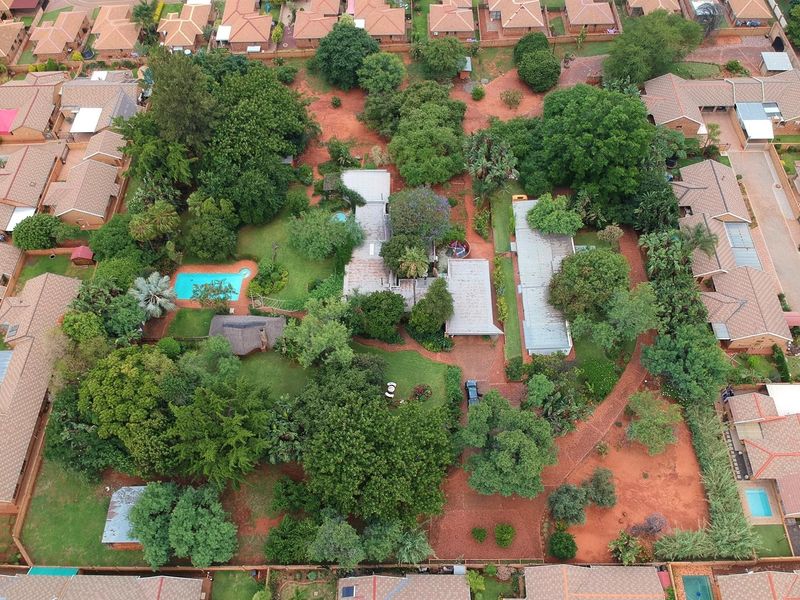 Aerial view of a spacious small holding property featuring a swimming pool, extensive mature gardens, and multiple residential structures within a residential estate.