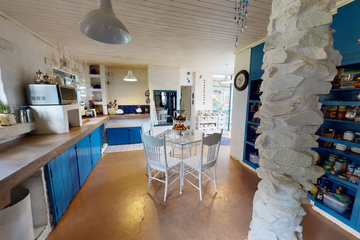 A rustic kitchen featuring blue built-in cabinetry, a prominent stone pillar, timber ceiling, and tiled backsplash, offering a unique character-filled space.