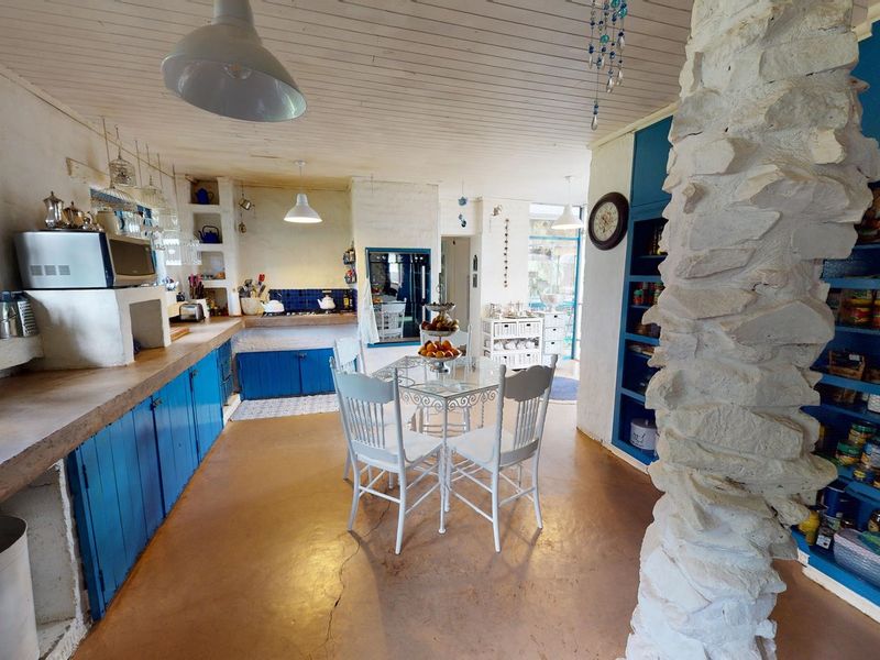 A rustic kitchen featuring blue built-in cabinetry, a prominent stone pillar, timber ceiling, and tiled backsplash, offering a unique character-filled space.