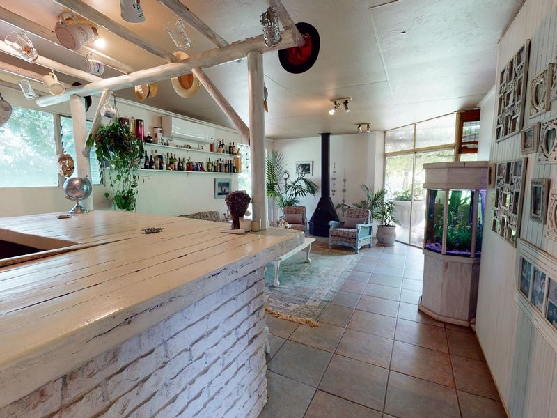 A rustic-style bar area featuring a brick-based counter, timber ceiling beams, tiled flooring, and a central fireplace, creating a cozy entertainment space.