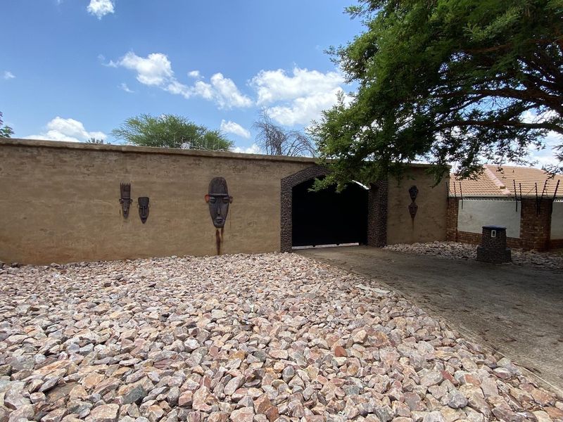 Front entrance view featuring a solid boundary wall with decorative elements, a gated driveway, and a low-maintenance rock garden.