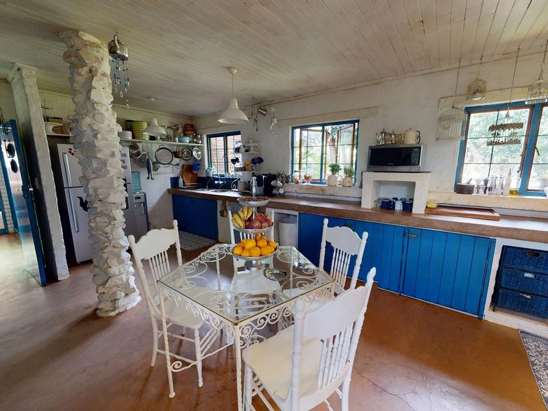 Rustic kitchen featuring a unique stone pillar, wooden ceiling, blue cabinetry, and ample counter space in a charming, lived-in small holding setting.