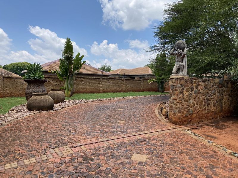 A well-maintained front entrance featuring a circular cobblestone driveway, stone boundary wall with electric fencing, and established garden landscaping.
