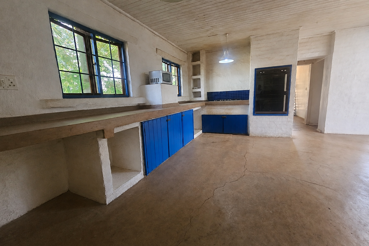 Spacious rustic kitchen featuring built-in concrete countertops, blue cabinetry, integrated oven, and hob, set within a character-filled space with a timber ceiling.
