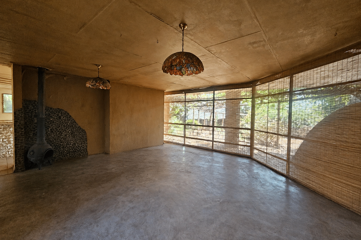 Spacious living area featuring a unique stone-clad fireplace, concrete flooring, and large windows with natural light, offering a rustic aesthetic ready for renovation.