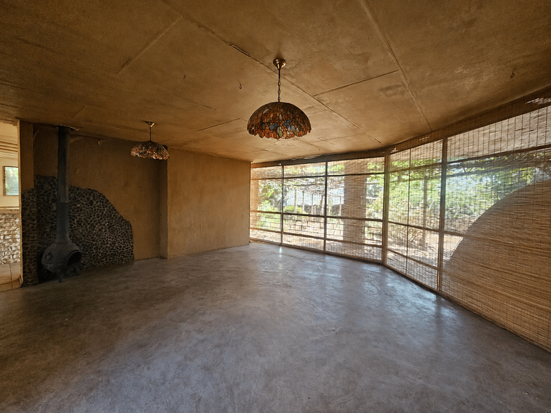 Spacious living area featuring a unique stone-clad fireplace, concrete flooring, and large windows with natural light, offering a rustic aesthetic ready for renovation.
