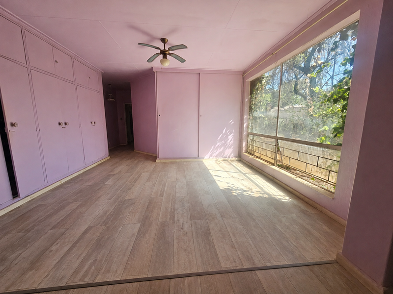 Spacious bedroom featuring extensive built-in cupboards, laminate flooring, a ceiling fan, and a large window providing natural light and garden views.