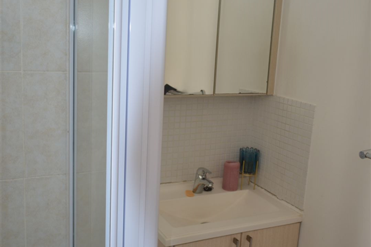 A compact bathroom featuring a shower enclosure, a wall-mounted vanity with a basin, and a mirrored medicine cabinet with tiled finishes.