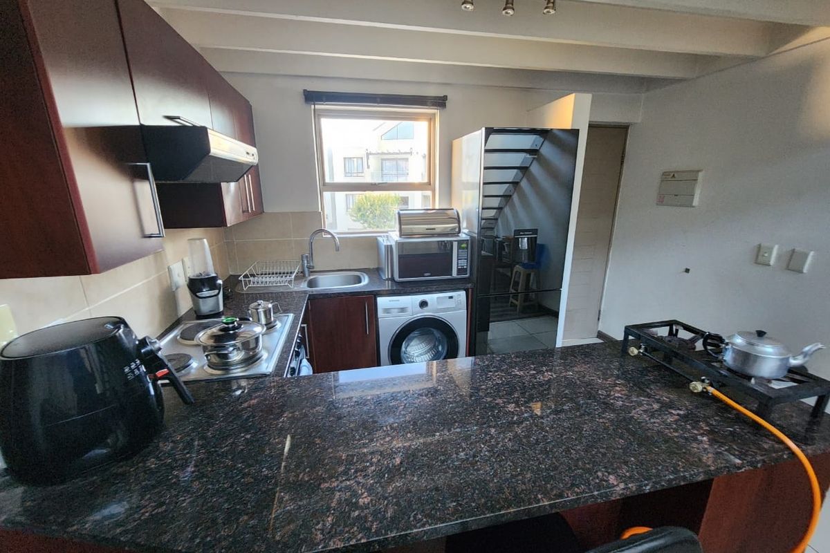 A functional kitchen featuring dark wood cabinetry, granite countertops, an integrated hob, and an extractor fan, with exposed ceiling beams and a breakfast bar.