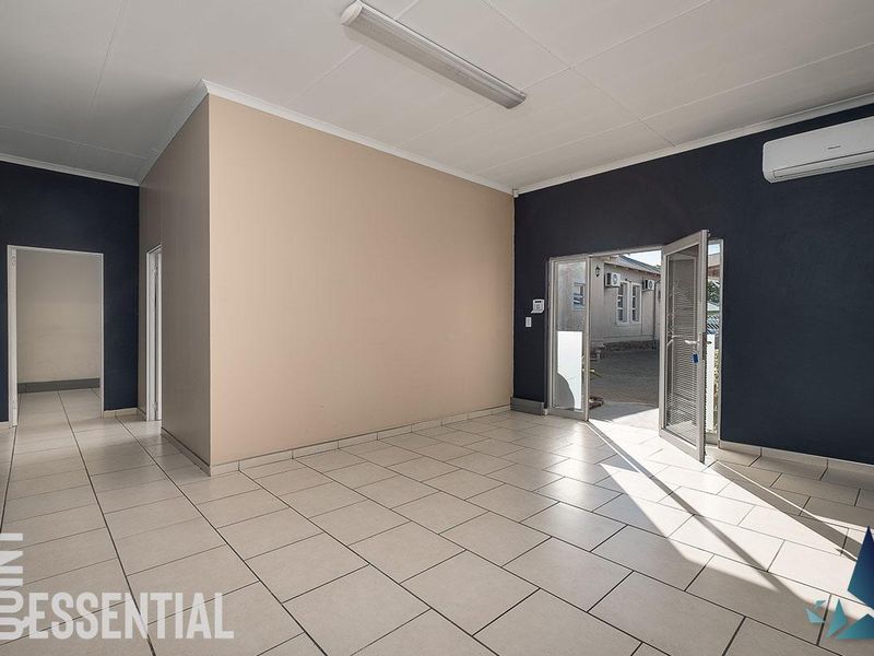 A bright, empty office space featuring tiled flooring, a wall-mounted air conditioning unit, and direct access to an outdoor area.