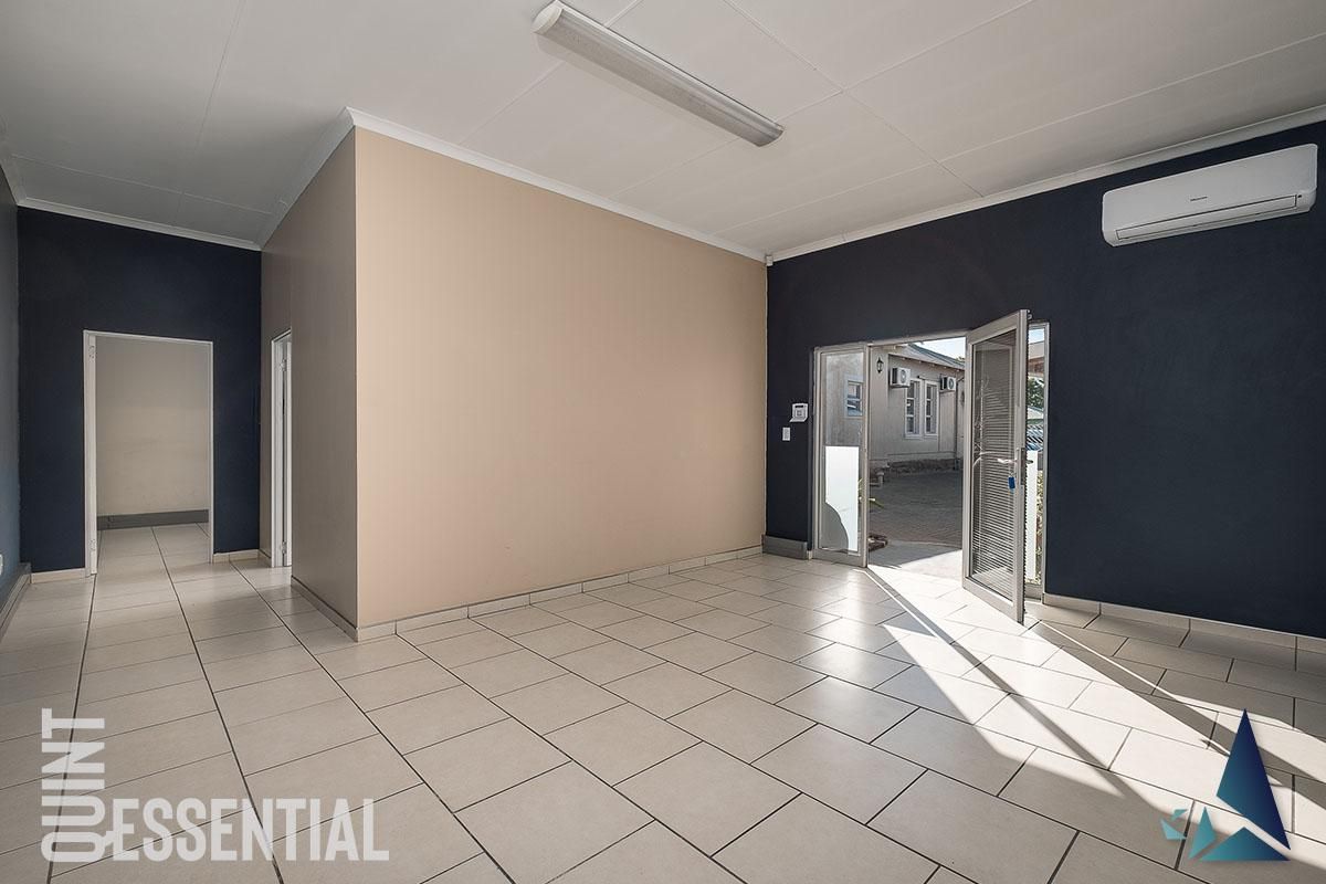 A bright, empty office space featuring tiled flooring, a wall-mounted air conditioning unit, and direct access to an outdoor area.