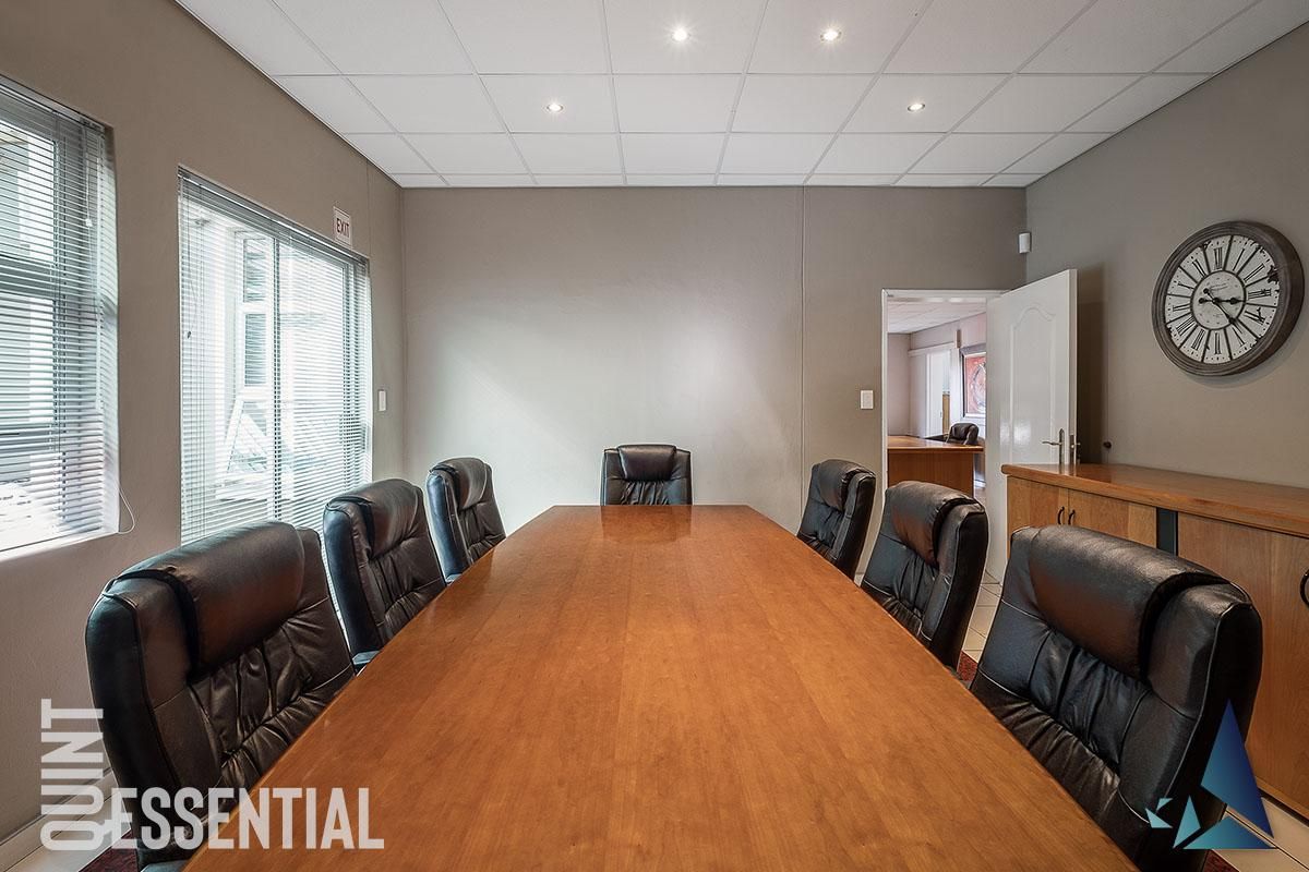 A professional boardroom or office space featuring a suspended ceiling with recessed lighting, venetian blinds, and built-in cabinetry.