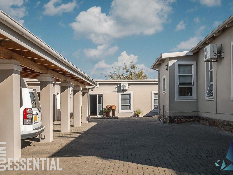A well-maintained paved courtyard area featuring a covered parking structure, exterior air conditioning units, and stone base detailing on the building facade.