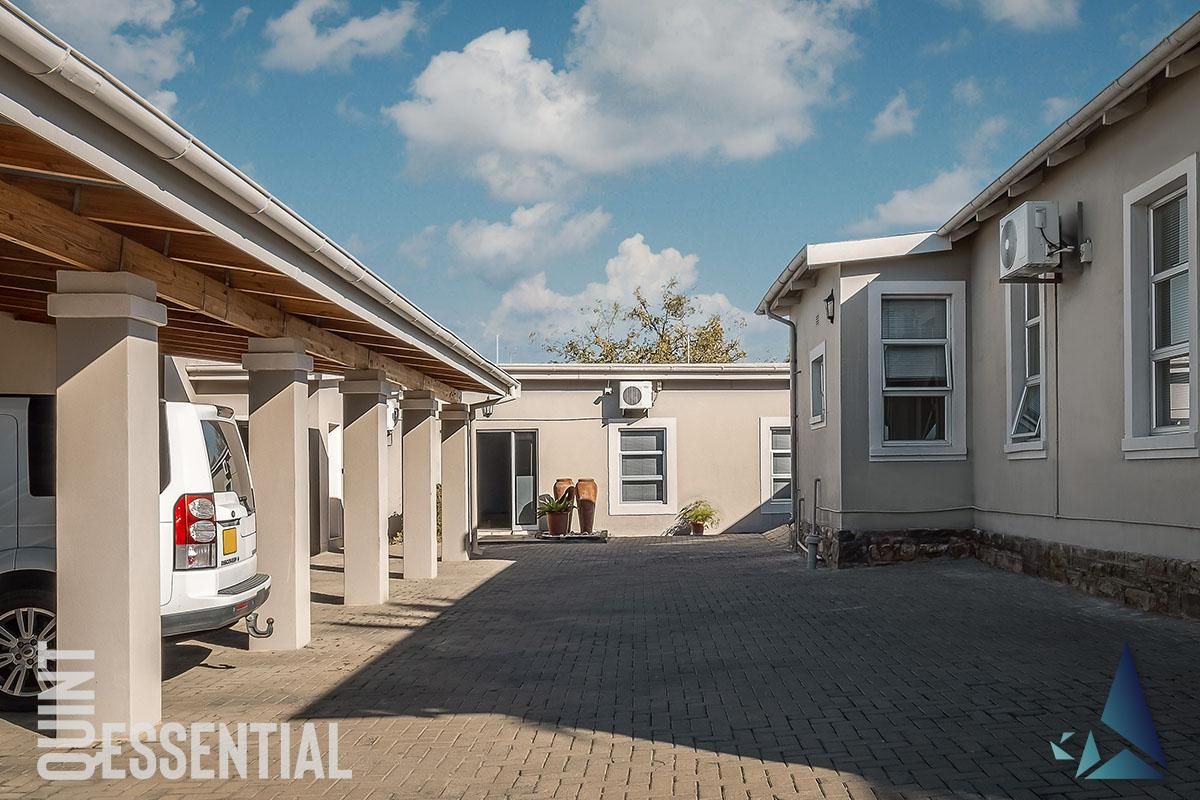 A well-maintained paved courtyard area featuring a covered parking structure, exterior air conditioning units, and stone base detailing on the building facade.
