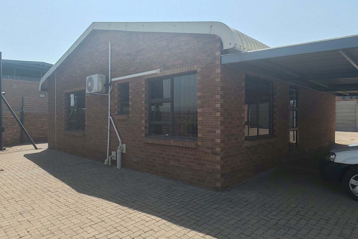 Exterior view of a commercial brick building featuring a metal carport, paved driveway, and wall-mounted air conditioning unit.