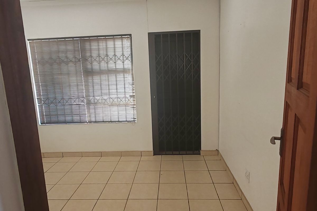 An empty room featuring tiled flooring, a window with fitted blinds, and a security gate at the entrance.