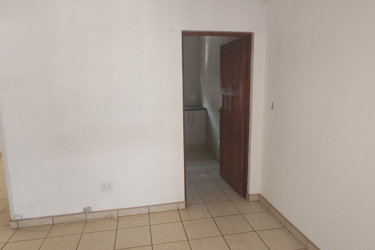 An empty interior space with tiled flooring and a wooden door leading to a small utility or kitchen area.