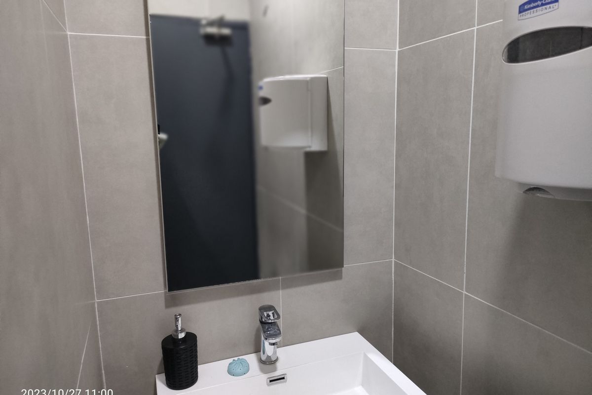 A modern industrial-style bathroom featuring large format grey wall tiles, a wall-mounted basin with chrome faucet, and a frameless mirror.