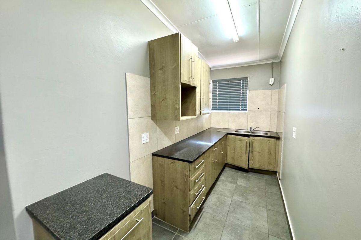 A functional kitchen area featuring wood-look cabinetry, dark countertops, tiled splashbacks, and a stainless steel sink.