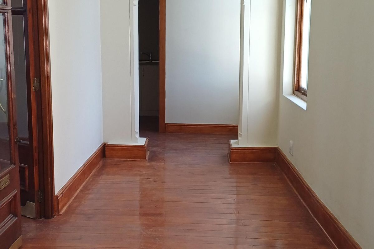 A bright, empty hallway featuring polished timber flooring, decorative ceiling cornices, and a classic architectural archway leading to an adjoining space.