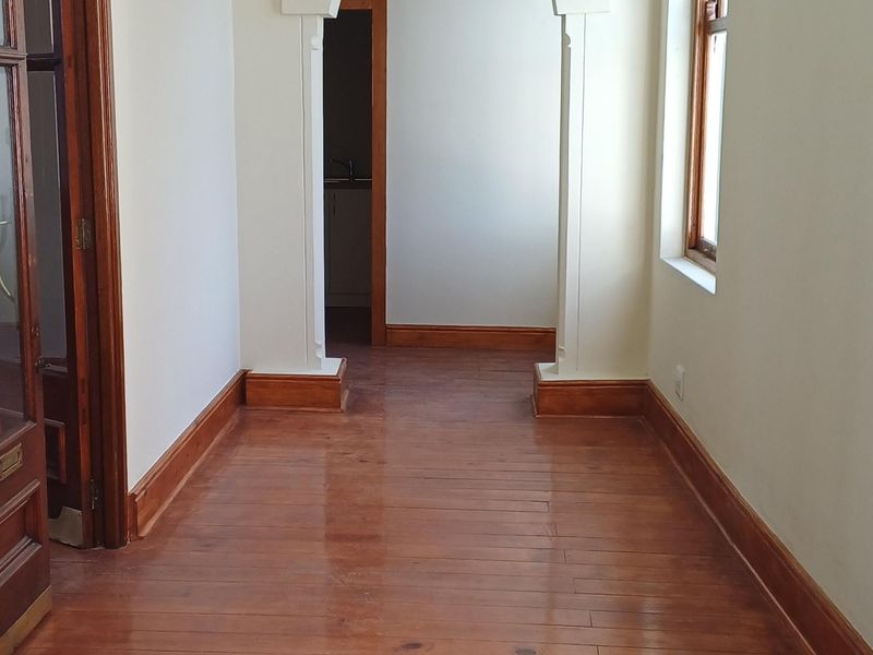 A bright, empty hallway featuring polished timber flooring, decorative ceiling cornices, and a classic architectural archway leading to an adjoining space.