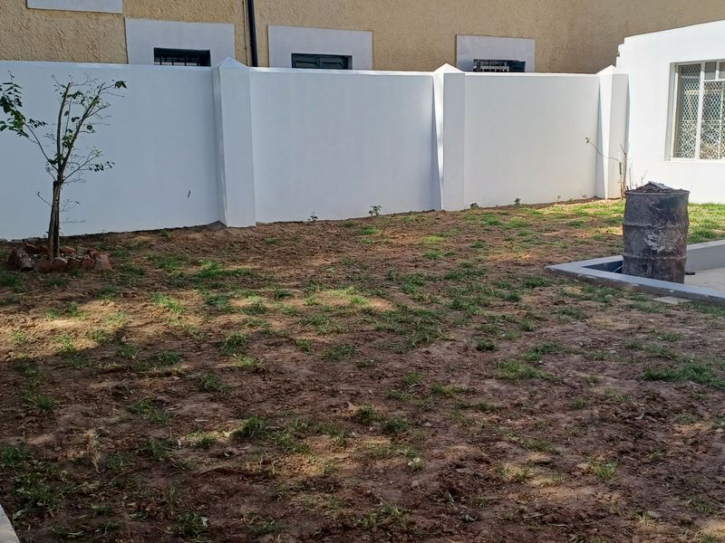 A rear outdoor area featuring a perimeter boundary wall and a concrete patio section, currently requiring landscaping and lawn maintenance.