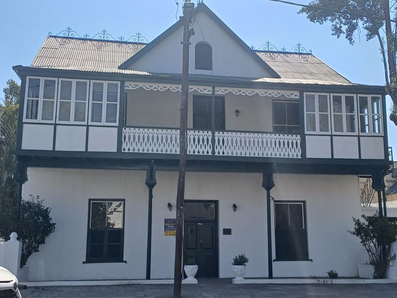 A historic two-story office building featuring a classic facade with a covered veranda, decorative timber fretwork, and traditional sash windows.