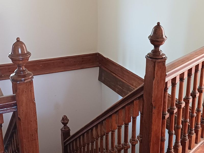 A classic wooden staircase featuring traditional balustrades, handrails, and newel posts, showcasing period architectural details in a hallway setting.