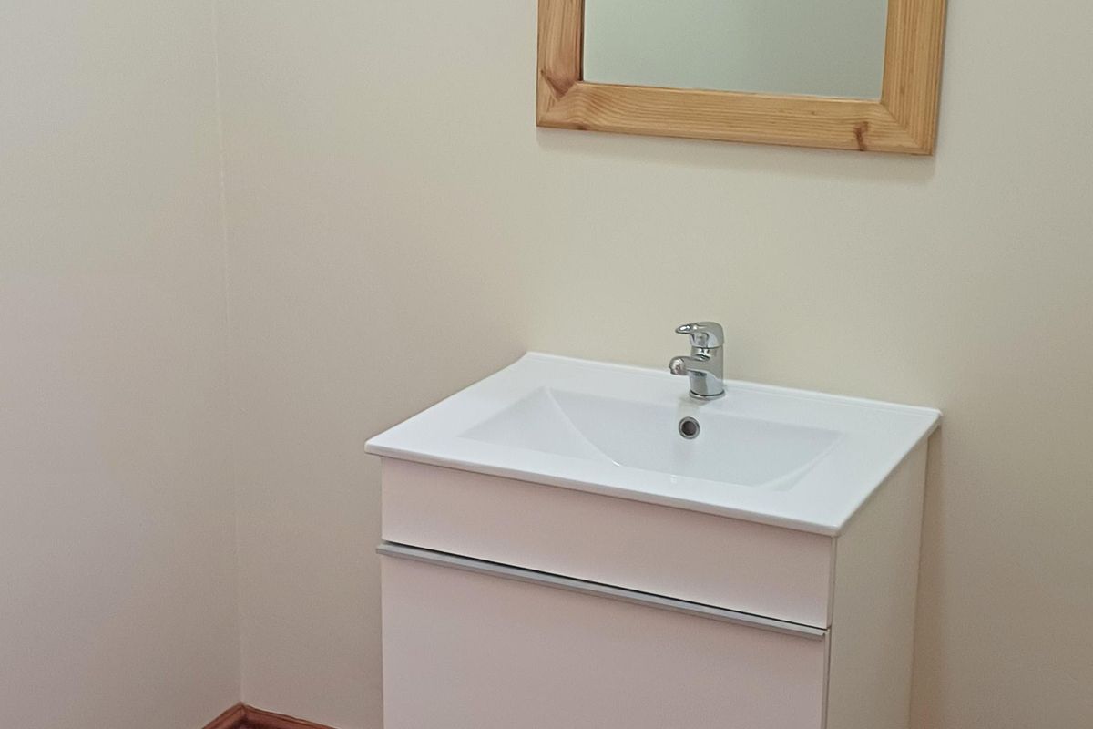 A clean, minimalist bathroom featuring a wall-mounted white vanity with an integrated basin, chrome tapware, and a timber-framed mirror above.
