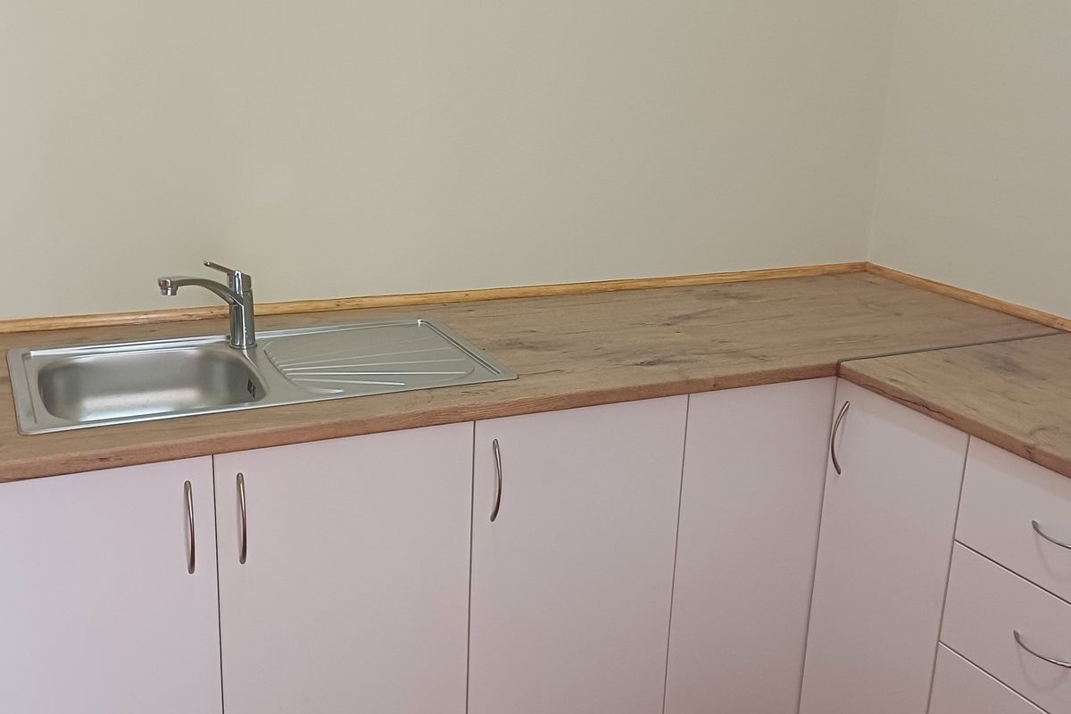 A clean, modern kitchenette area featuring light-toned base cabinetry, wood-effect laminate countertops, and a stainless steel sink with a fitted faucet.