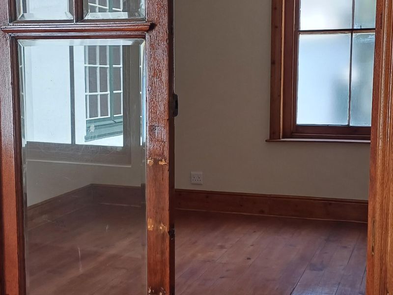 An empty office space featuring polished hardwood flooring, a classic timber sliding door, and a traditional wrought iron chandelier.