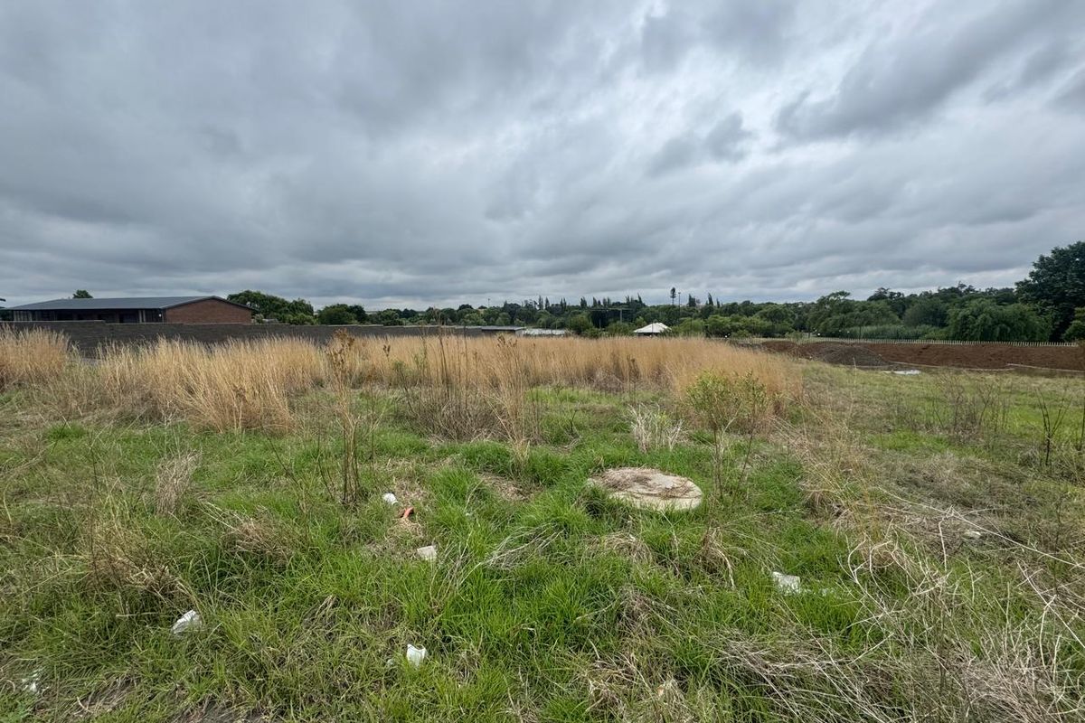 A view of a vacant commercial land plot featuring natural grass cover and a concrete utility access cover.