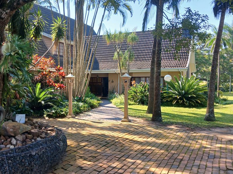 A charming front entrance view of the small holding, featuring a brick-paved pathway, mature garden landscaping, and a well-maintained tiled roof structure.