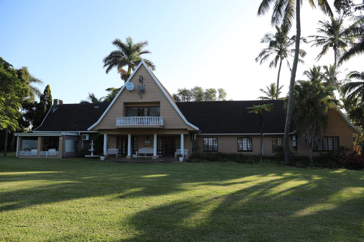 A spacious rear view of the property featuring a large lawn, covered patio, and a distinctive A-frame architectural design with a balcony.