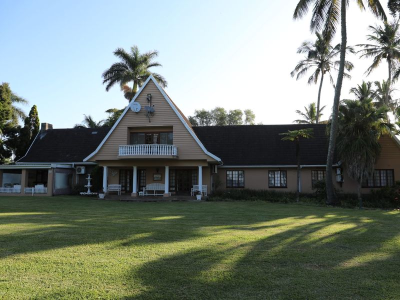 A spacious rear view of the property featuring a large lawn, covered patio, and a distinctive A-frame architectural design with a balcony.