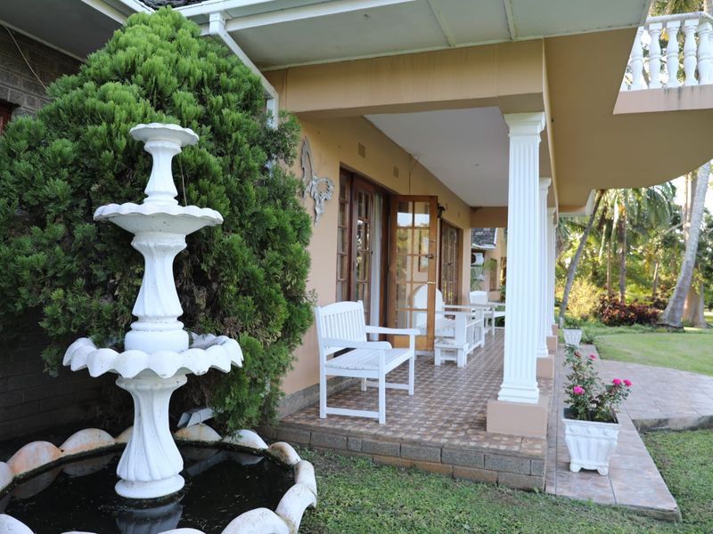 A covered patio area featuring tiled flooring, decorative columns, and access to the garden, complemented by a classic water fountain.